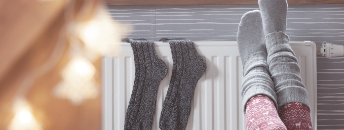 piernas de mujer con calcetines sobre un calefactor frente a una ventana por la que se ven pinos