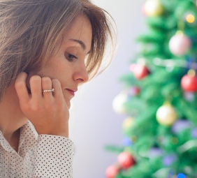 mujer pensativa con mano en el rostro mira hacia abajo; de fondo un árbol de navidad