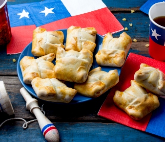 empanadas chilenas sobre plato azul y servilletas y vasos con diseño de bandera chilena