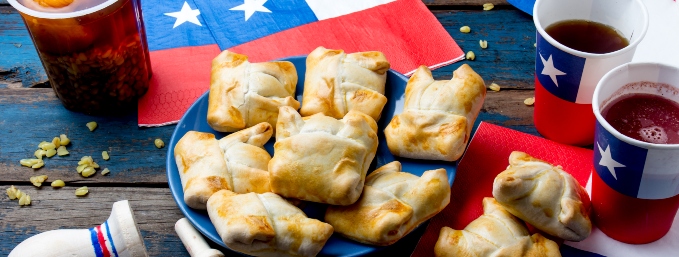 empanadas chilenas sobre plato azul y servilletas y vasos con diseño de bandera chilena