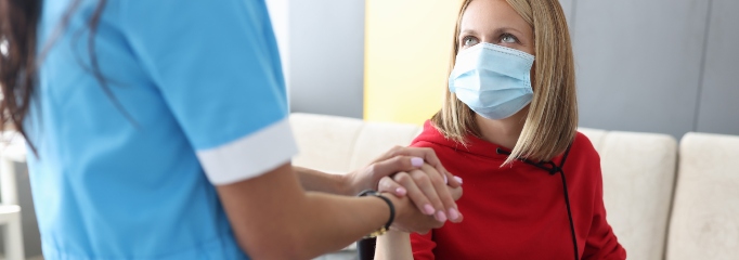 mujer con mascarilla mira a enfermera que le da la mano
