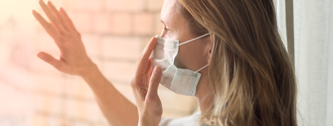 mujer rubia con mascarilla mira a través de la ventana