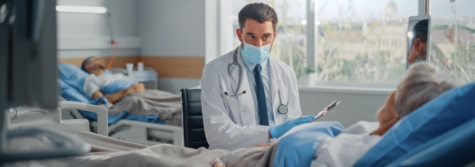médico con mascarilla conversa con paciente mayor que se recupera en una cama