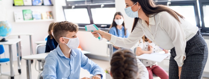 profesora con mascarilla toma temperatura a alumnos con termómetro digital en sala de clases