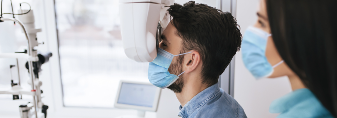hombre joven con mascarilla se realiza un examen de oftalmología al lado de una doctora