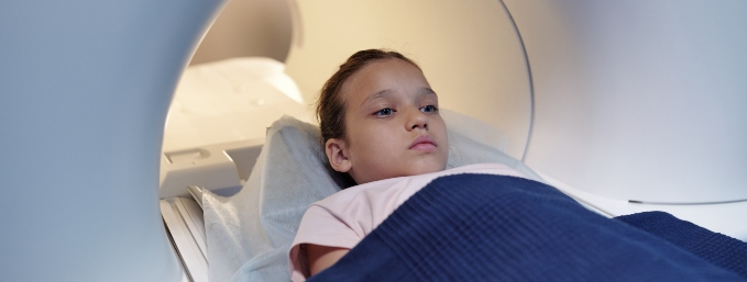 niña acostada en máquina de procedimientos de imágenes de tomografía, TAC o scanner, tapada con manta azul