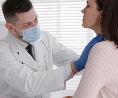 médico con mascarilla examina glándula tiroides de paciente mujer